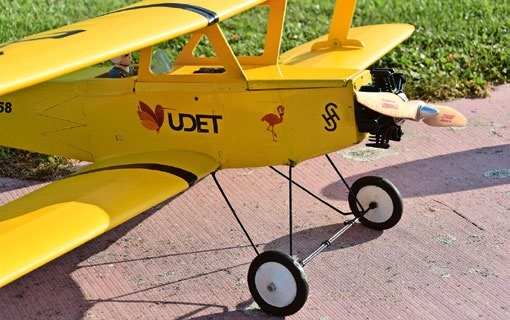 A yellow model aircraft (Udet Flamingo) on a paved surface. The model is a biplane with 'UDET' and a flamingo logo on the side.