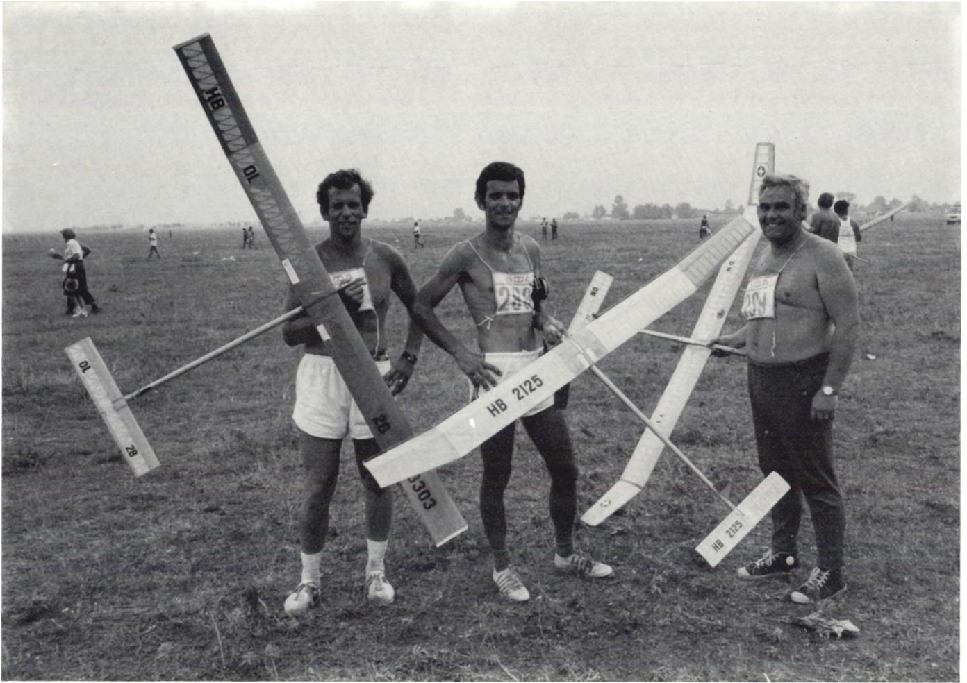 Three men holding model gliders in a field.