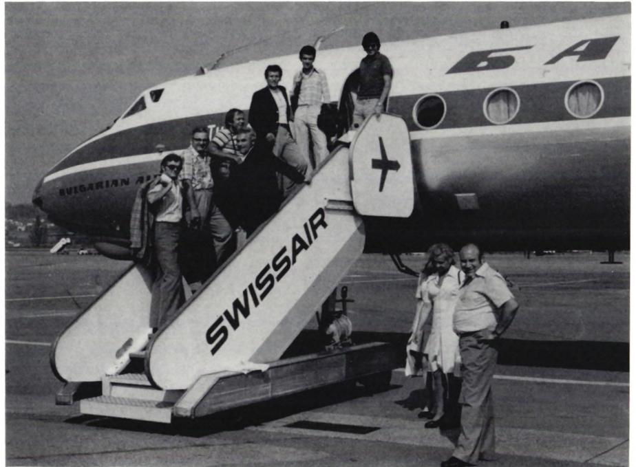 Black and white photograph of a Swissair airplane on the tarmac. A group of people, including team members and supporters, are standing on the stairs leading up to the plane. The plane has 'SWISSAIR' and 'БГ' (Bulgarian Air) markings.