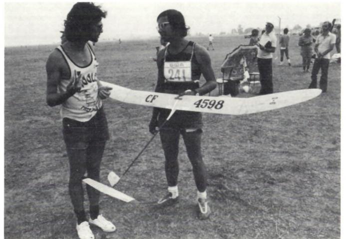 Two men holding a model glider in a field.
